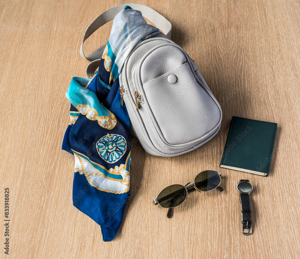 grey shoulder bag on a wooden background, a neck scarf, a watch, a notebook and sunglasses grey shoulder bag on a wooden background, a neck scarf, a watch, a notebook and sunglasses