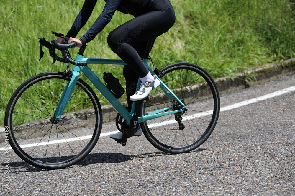 legs of Cliclist in tight cycling shorts and black leggings pedaling on a road bike during a road race legs of Cliclist in tight cycling shorts and black leggings pedaling on a road bike during a road race