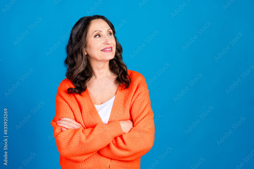 Photo portrait of gorgeous senior woman crossed hands look empty space wear trendy orange outfit hairdo isolated on blue color background Photo portrait of gorgeous senior woman crossed hands look empty space wear trendy orange outfit hairdo isolated on blue color background