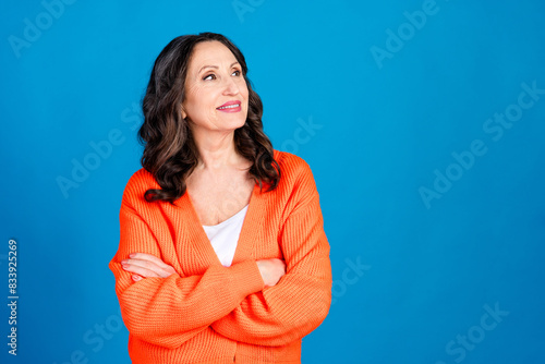 Photo portrait of gorgeous senior woman crossed hands look empty space wear trendy orange outfit hairdo isolated on blue color background