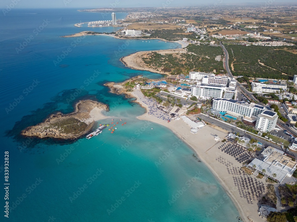 Fototapeta premium Panoramic view of Nissi Bay and the landscape. Sandy beach with Nissi island and hotel resorts in Ayia Napa. Aerial view of the Famagusta coastline towards Ayia Napa Marina. Calm sunny morning.