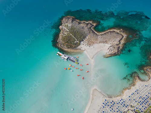 Obraz na płótnie Aerial view of Nissi island and empty beach in Ayia Napa, Cyprus. Calm turquoise Mediterranean sea on a quiet sunny morning. No people. Sandy beach with lines of parasols and watersports business. w salonie