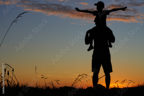 silhouettes of father carries his son on his back standing at sunset. concept of father s day