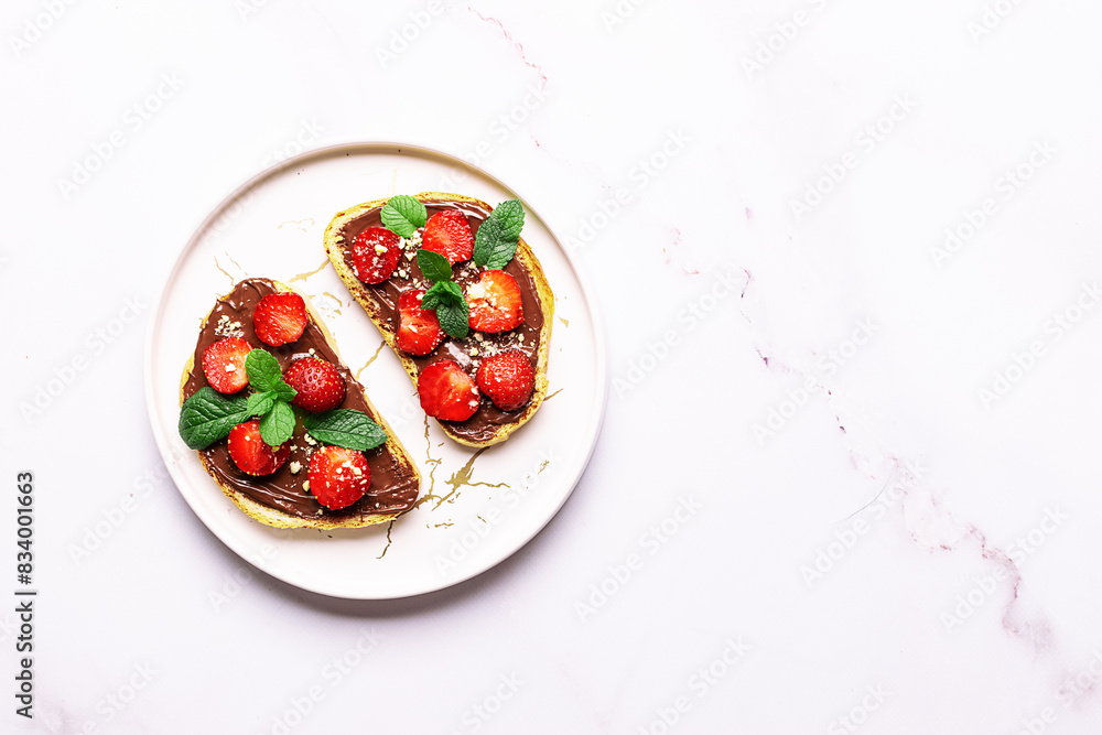 Sweet homemade toasts with chocolate paste, nuts, srtawberry and aromatic mint leaves on the serving plate on white marble background. Tasty summer dessert. Sweet homemade toasts with chocolate paste, nuts, srtawberry and aromatic mint leaves on the serving plate on white marble background. Tasty summer dessert.