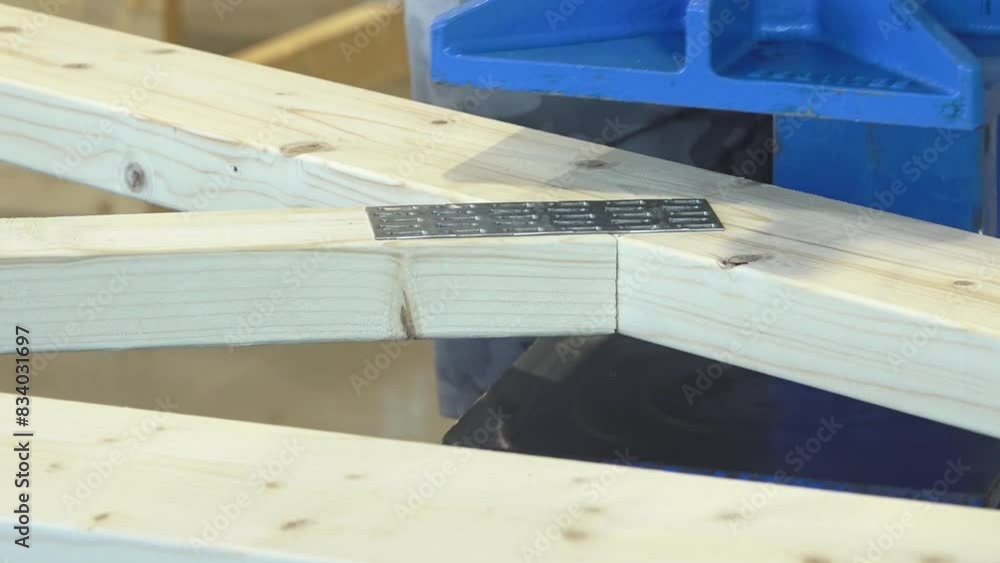 Balvi, Latvia - May 25, 2024 - Machine pressing metal plates into intersecting wooden beams, showing construction process. Balvi, Latvia - May 25, 2024 - Machine pressing metal plates into intersecting wooden beams, showing construction process.