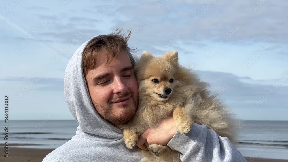 Happy young man walking with his Pomeranian spitz dog, hold puppy on hands on the beach at summer sunny day. Happy young man walking with his Pomeranian spitz dog, hold puppy on hands on the beach at summer sunny day.