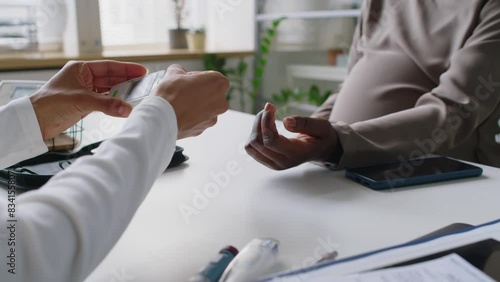 Close-up shot of hands of anonymous healthcare practitioner teaching unrecognizable pregnant black woman with diabetes how to prick finger with lancet and measure blood glucose with meter photo