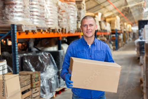 Positive warehouse worker dragging boxes on his hands © JackF