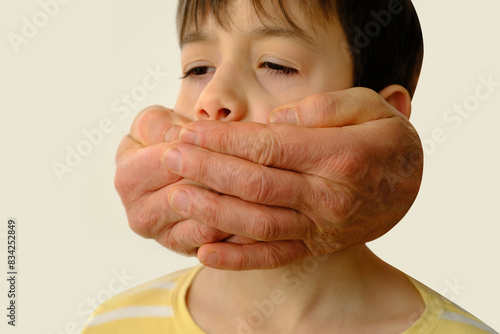 closeup rude male hands cover the mouth of a child, a boy suffers from violence, concept of parenting, punishment for bad words, children's jokes, teasing, ban on his opinion photo