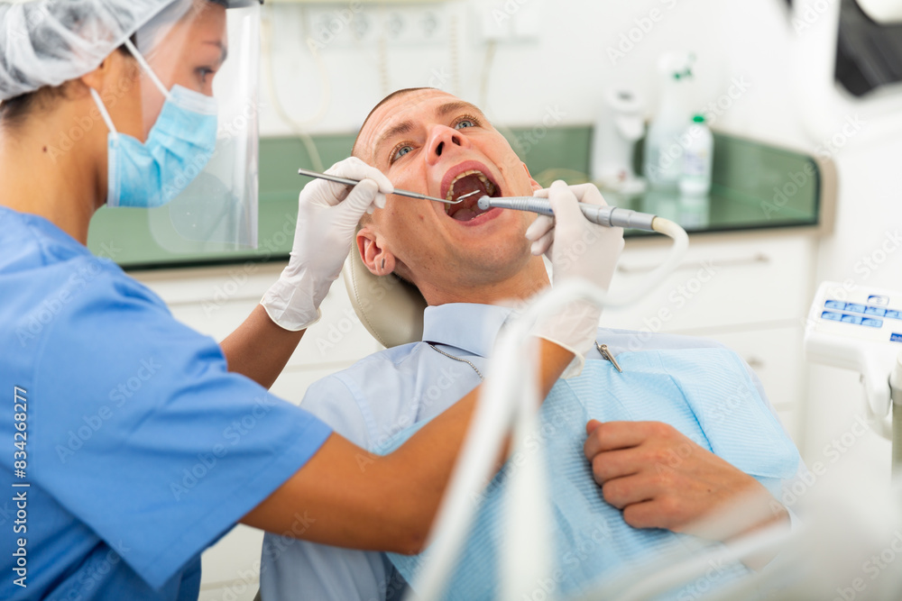 Dentist is treating male patient which is sitting in dental chair in clinic