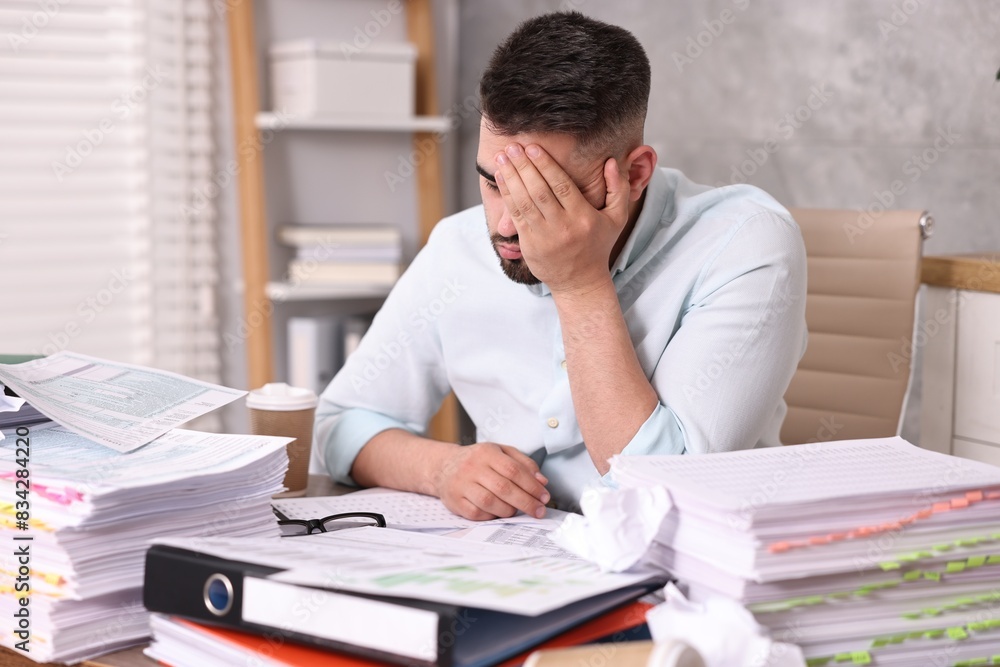 Overwhelmed man surrounded by documents at workplace in office Overwhelmed man surrounded by documents at workplace in office