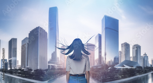 日本の街・都市・朝日を受けたオフィスビル群を前に佇み風を受けて髪をなびかせる会社員の女性の出勤　ビジネス・はじまり・決意・目標・挑戦のイメージ © tenpadasi