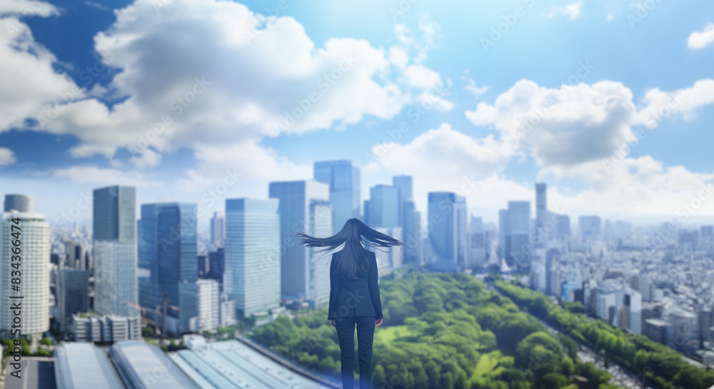 Fototapeta premium 日本の街・都市・朝日を受けたオフィスビル群を前に佇み風を受けて髪をなびかせる会社員の女性の出勤 ビジネス・はじまり・決意・目標・挑戦のイメージ