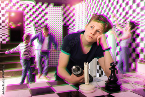 Quadro em tela Portrait of thoughtful teenage boy trying to find solution of conundrum in quest room stylized under chessboard