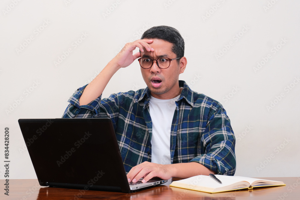 A man on his working place looking to laptop with shocked expression A man on his working place looking to laptop with shocked expression