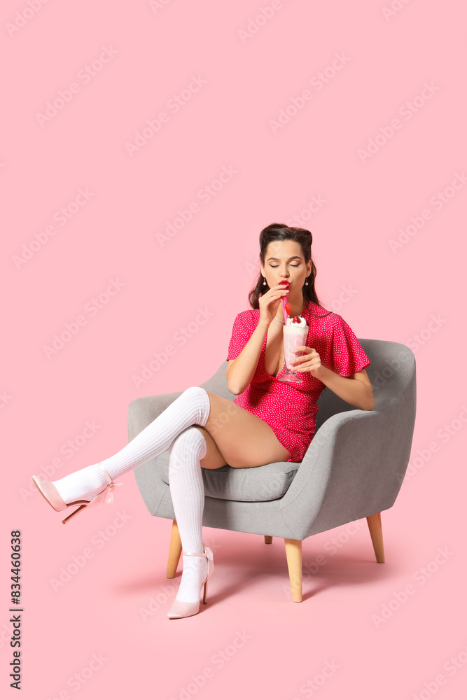 Portrait of beautiful pin-up woman with strawberry smoothie sitting on armchair on pink background Portrait of beautiful pin-up woman with strawberry smoothie sitting on armchair on pink background