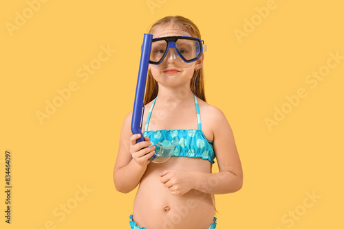 Cute little girl in swimsuit with snorkeling mask on yellow background