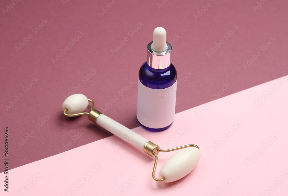 Massage roller and serum bottle for anti-aging facial massage on a pink burgundy background Massage roller and serum bottle for anti-aging facial massage on a pink burgundy background