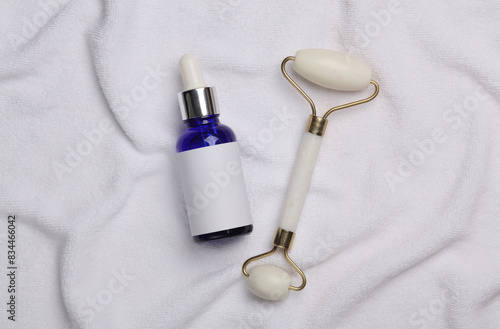 Jade facial roller with serum bottle on white towel. Beauty concept. Top view