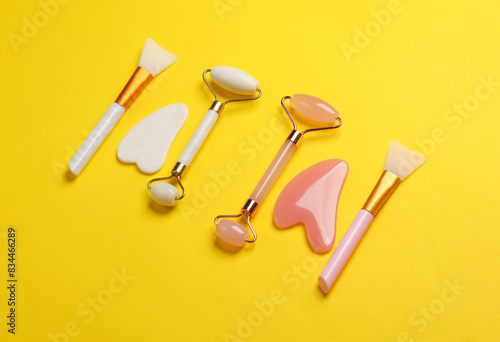 Jade facial rollers and gua sha scrapers on yellow background. Beauty concept