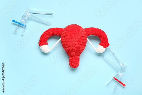 Knitted uterus with gynecological speculums on blue background photo
