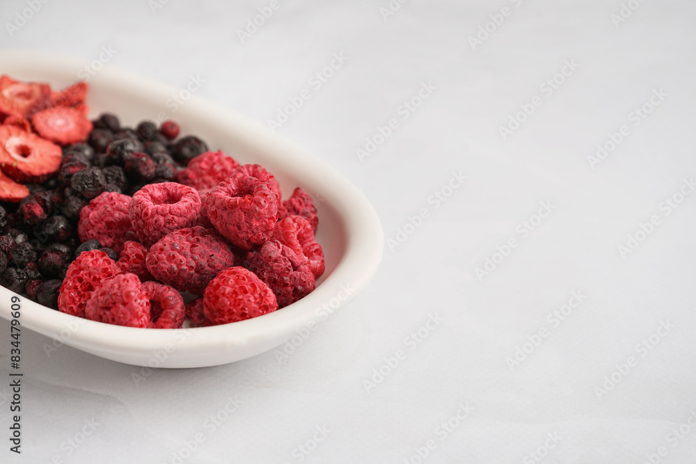 Bowl with tasty freeze-dried raspberries, strawberries and blueberries on white background Bowl with tasty freeze-dried raspberries, strawberries and blueberries on white background