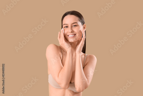 Photography Young woman with cotton pad removing makeup on brown background