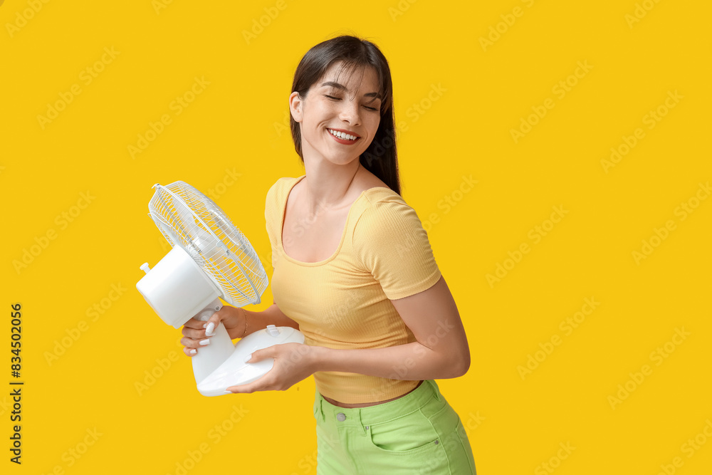 Young woman with electric fan on yellow background Young woman with electric fan on yellow background
