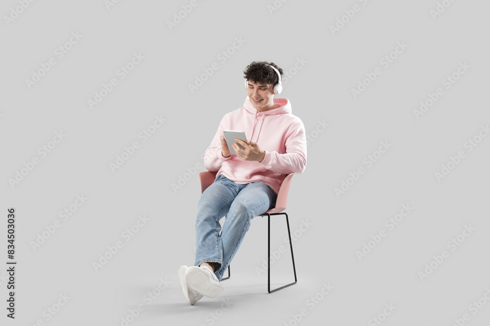 Handsome young man with headphones using tablet computer in armchair on light background Handsome young man with headphones using tablet computer in armchair on light background
