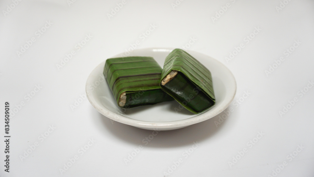 Lemper, a traditional snack from Indonesia, made from sticky rice, steamed with coconut milk, chicken floss inside, and wrapped with banana leaf. Served on white plate, isolated on white background Lemper, a traditional snack from Indonesia, made from sticky rice, steamed with coconut milk, chicken floss inside, and wrapped with banana leaf. Served on white plate, isolated on white background