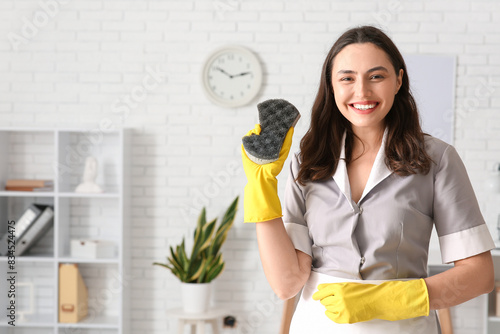 Young chambermaid with cleaning sponge in office