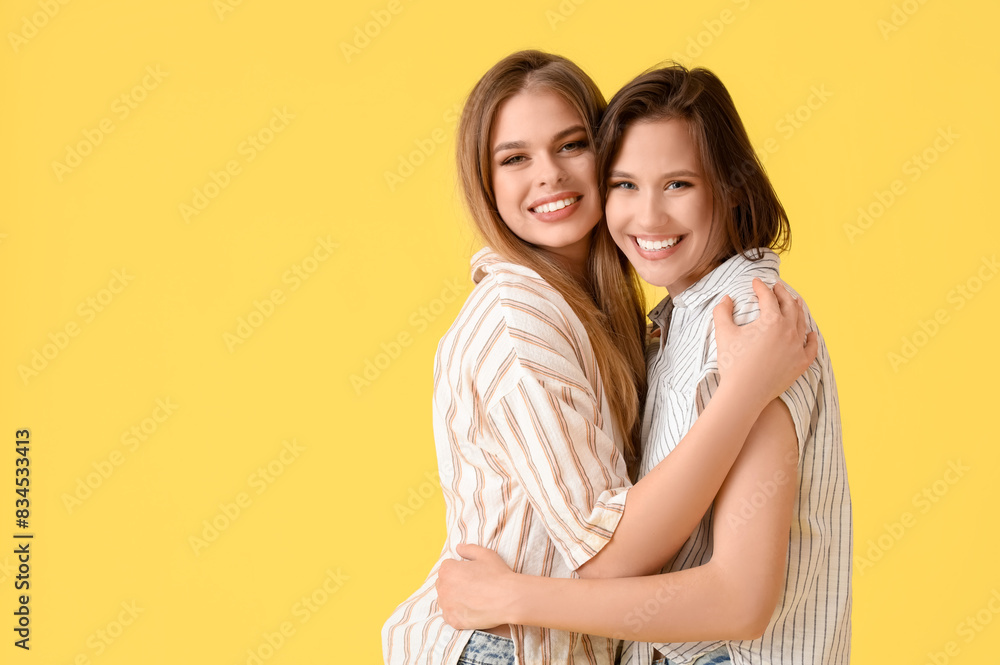 Female friends hugging on yellow background Female friends hugging on yellow background