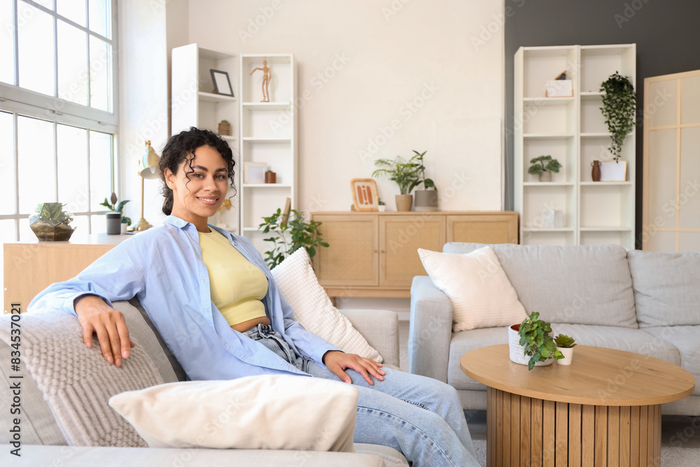 Young African-American woman sitting on grey couch at home Young African-American woman sitting on grey couch at home