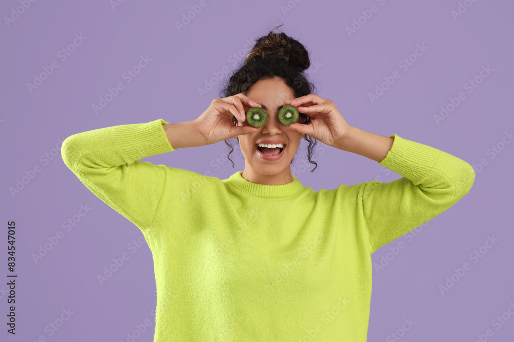 Beautiful young happy African-American woman with slices of kiwi on purple background Beautiful young happy African-American woman with slices of kiwi on purple background
