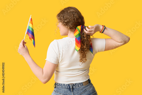 Young woman with LGBT flag and hairscarf on yellow background, back view photo