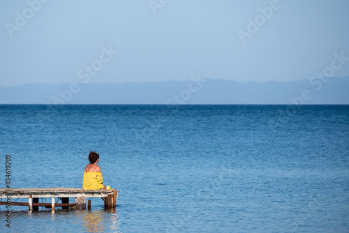 A woman sits alone on a dock and enjoys watching the sea