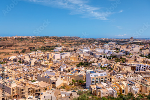  Scenic view of Victoria city from Gozo island in Malta. Cityscape with numerous buildings under a clear blue sky