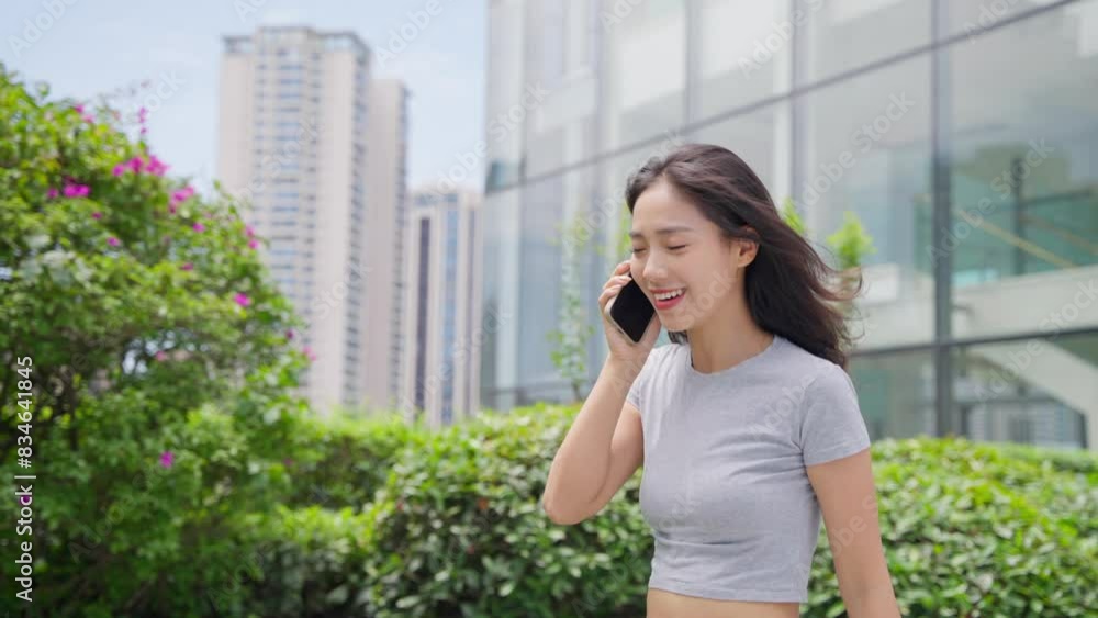 Charming young asian woman talking on the mobile phone walking in the urban city park Charming young asian woman talking on the mobile phone walking in the urban city park
