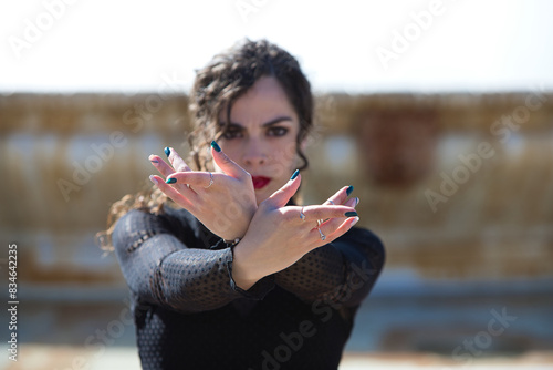 Beautiful woman dancing flamenco in a square in Seville, Spain. She wears a typical black dress and shows her hands strongly to the camera. Focus on hands and face out of focus.