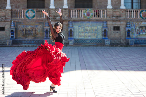 Beautiful woman dancing flamenco in a square in Seville, Spain. She is wearing a typical red and black gypsy dress and dancing flamenco with a lot of art. Flamenco, cultural heritage of humanity.