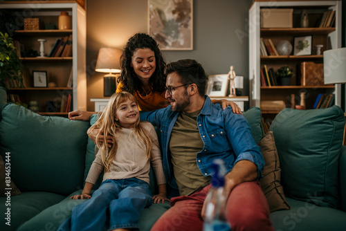 Smiling parents with their daughter enjoying quality time on the living room sofa photo