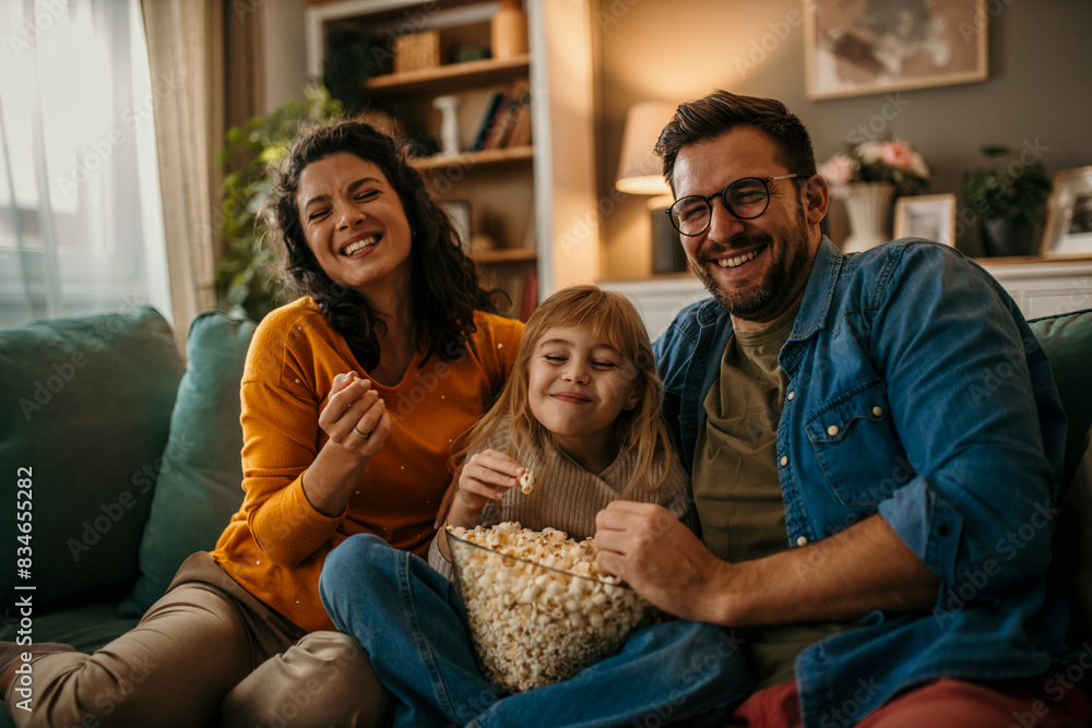 Smiling Caucasian family sitting on the couch and watching a comedy on the TV Smiling Caucasian family sitting on the couch and watching a comedy on the TV