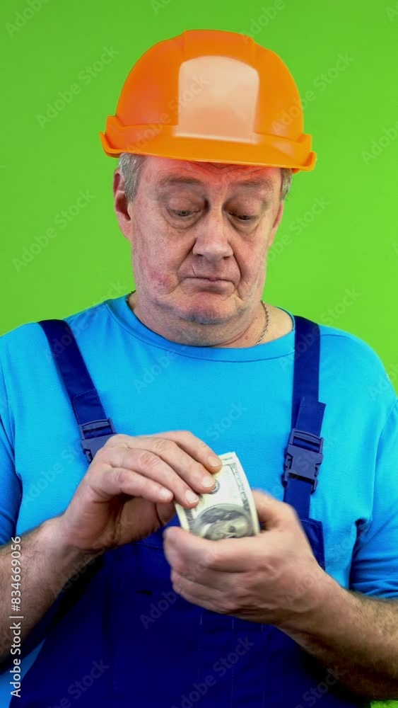 Senior construction worker in overalls counting dollars and puts it in pocket. Senior construction worker in overalls counting dollars and puts it in pocket.