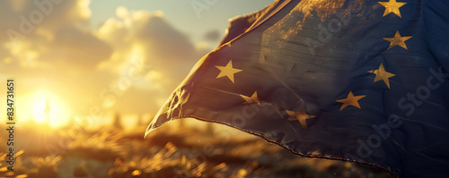 The European Union flag flutters in the wind against a beautiful field of stunning sky with clouds at a beautiful warm sunset. Background for design.