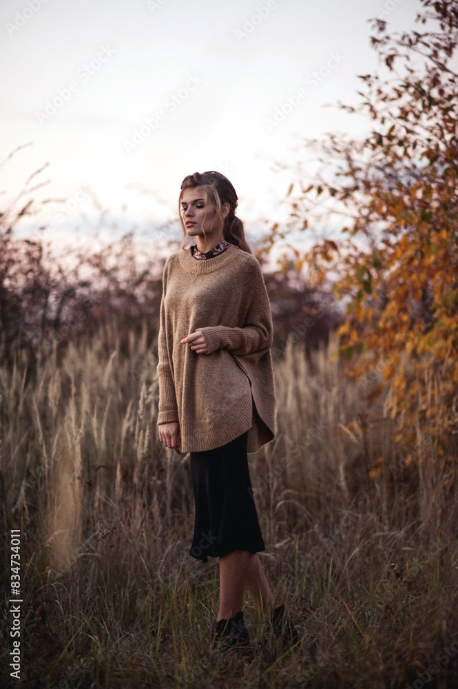 Outdoor fashion photo of young beautiful girl in knitted sweater and black skirt posing outdoor on nature background in autumn. Fine art Outdoor fashion photo of young beautiful girl in knitted sweater and black skirt posing outdoor on nature background in autumn. Fine art