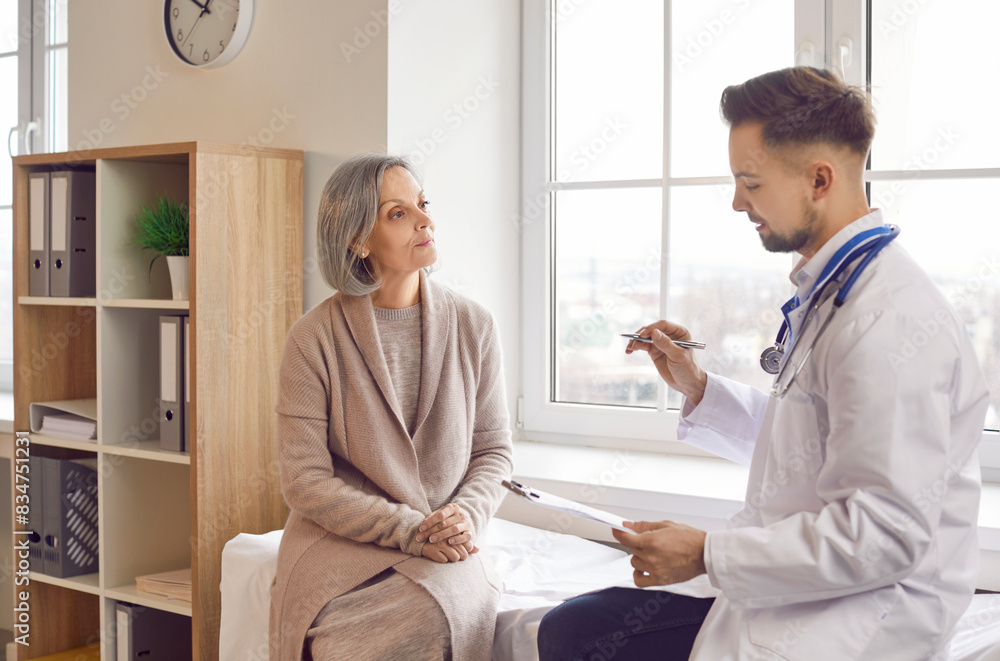 Fototapeta premium Caucasian male doctor or nurse consulting an elderly patient during a visit to the hospital office. The medical professional provides care and assistance to the senior, old individual.