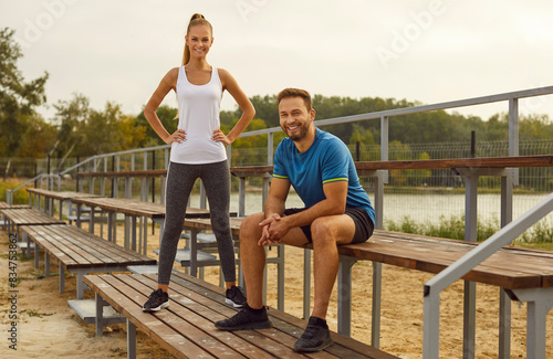Portrait of sporty happy young couple wearing sportswear standing in city park and looking cheerful at camera after sport fit exercises in nature. Workout and fitness outdoors concept.