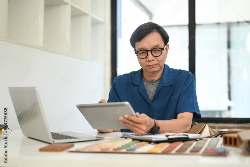 Middle age man interior designer sitting in front of laptop and using digital tablet at workplace Middle age man interior designer sitting in front of laptop and using digital tablet at workplace