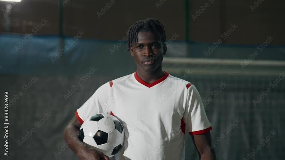 Happy young black soccer player playing with ball on indoors field, portrait. African American athletic man throwing ball, hitting by head, smiling and laughing, workout of professional football team Happy young black soccer player playing with ball on indoors field, portrait. African American athletic man throwing ball, hitting by head, smiling and laughing, workout of professional football team