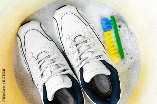Cleaning white sneakers with a brush and detergent in a basin. © Natallia